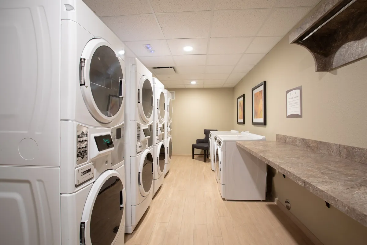 A bright, well-maintained laundry room featuring multiple washing machines and dryers, a convenient folding area, and colorful artwork on the wall. The space feels inviting and practical, with families or individuals attending to their laundry needs in a relaxed atmosphere.