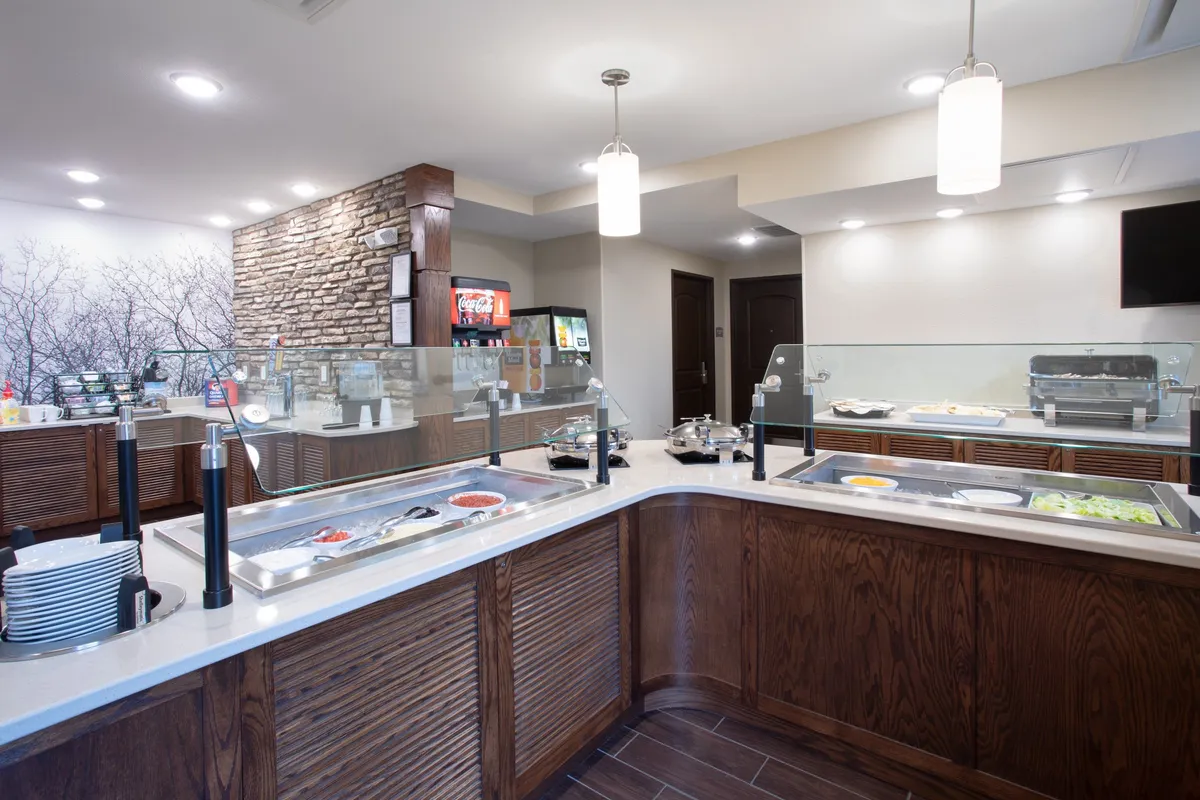 A bright, welcoming breakfast area displaying a buffet counter with a diverse food display, coffee machine, and beverage station. The atmosphere is casual and sociable, suggesting a space where guests can enjoy a complimentary breakfast or gather for a snack.