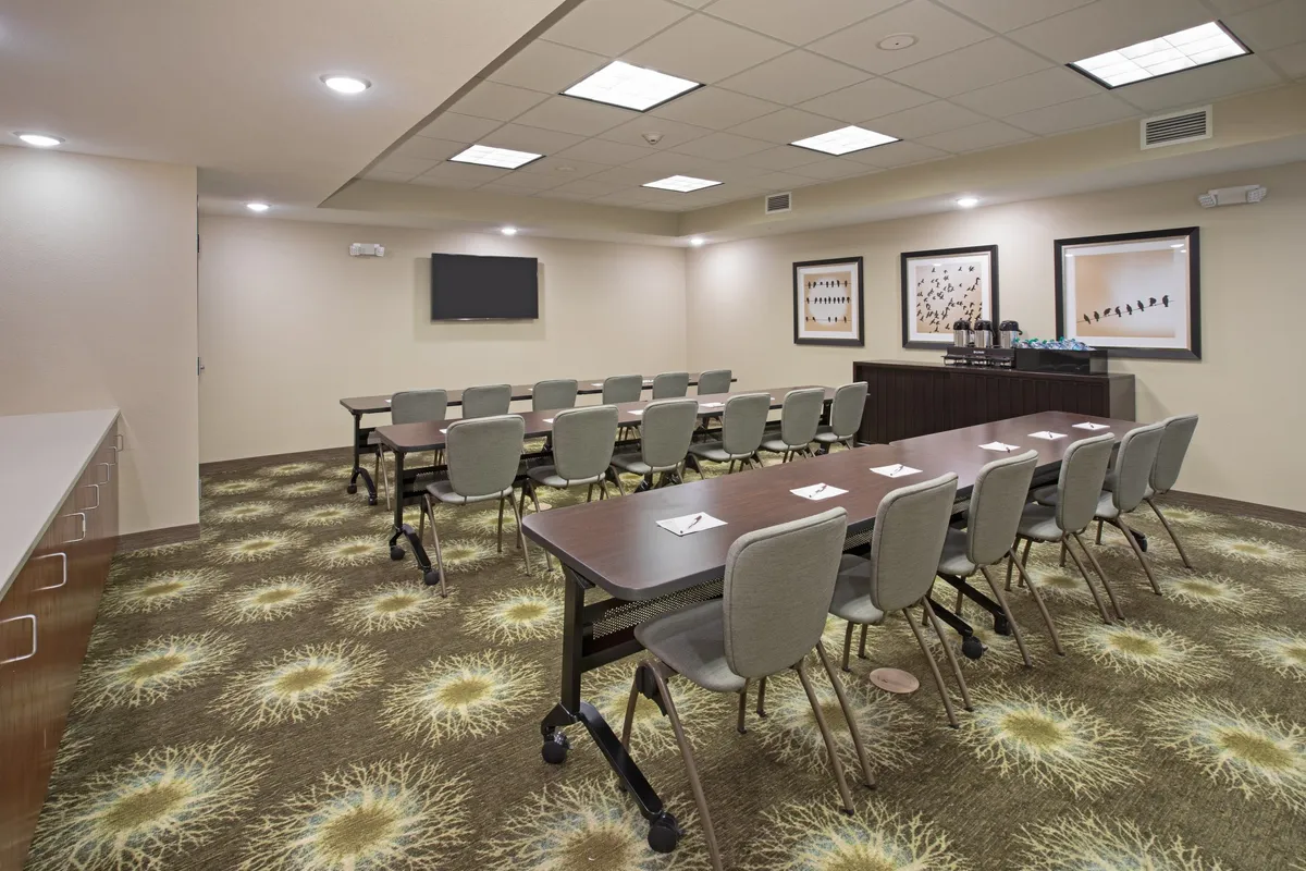 A contemporary business center with a long conference table, artwork on the walls, a television screen for presentations, and a well-stocked refreshment station. The room is designed to foster collaboration and productivity.