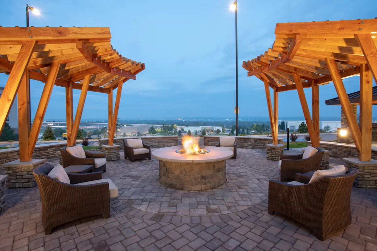 A communal outdoor seating area under wooden pergolas, centered around a glowing fire pit. Guests are pictured socializing, sharing meals, or simply enjoying a peaceful evening under the open sky.