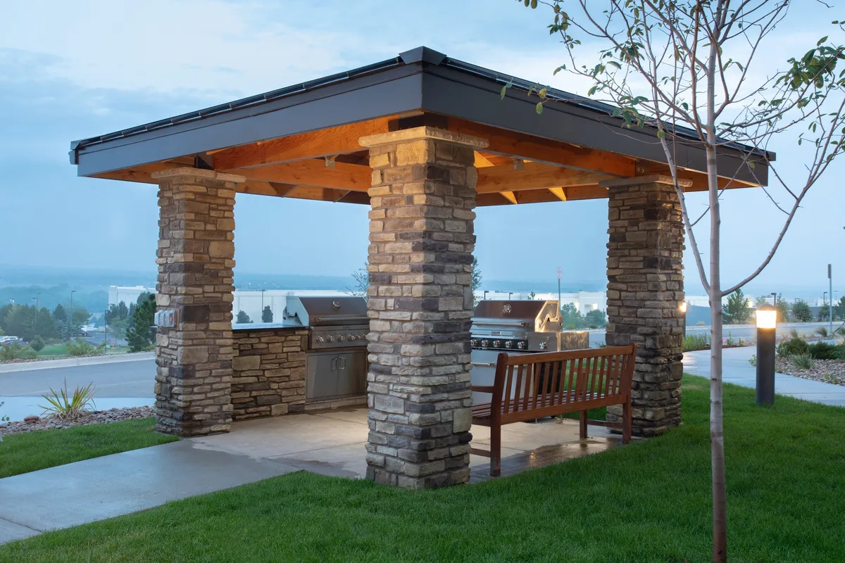 This image showcases the inviting stone grill area surrounded by a landscaped garden, featuring a wooden bench for relaxing and social gatherings. The outdoor setting highlights opportunities for guests to unwind, barbecue, and enjoy memorable moments in a communal environment.