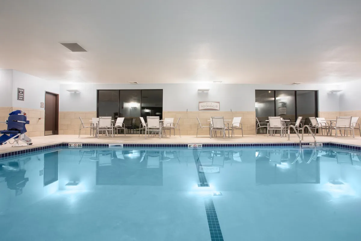 The serene indoor swimming pool features large windows letting in natural light, with lounge chairs for relaxation. The inviting setting is ideal for unwinding after a day out, whether taking a swim under soft lighting or enjoying a peaceful moment by the pool.