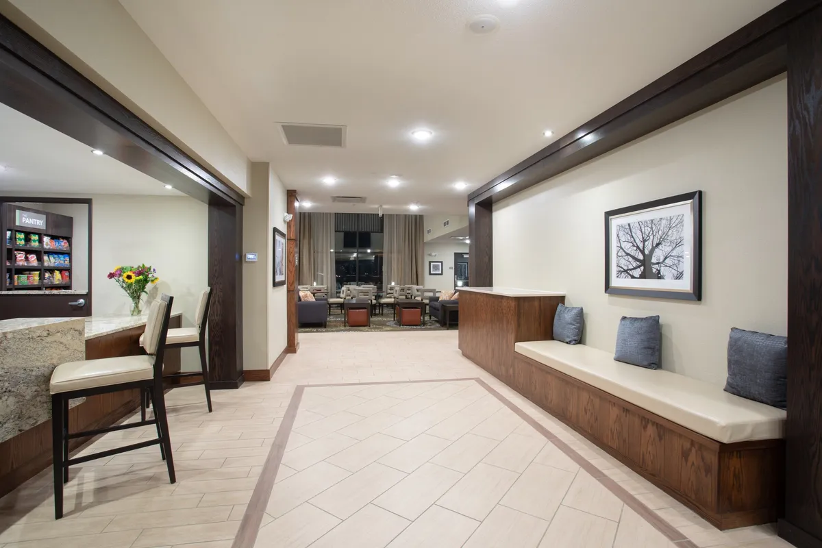 A comfortable interior space with a plush seating area near the front desk, brightened by natural light from large windows. Decorative artwork and a communal atmosphere create an inviting spot to unwind or casually check emails.