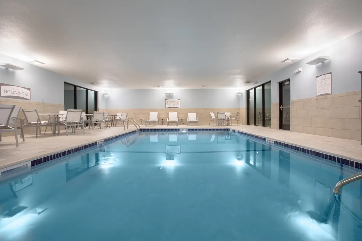 A tranquil indoor swimming pool scene featuring sparkling blue water, several comfortable lounge chairs along the poolside, and large windows that allow natural light to filter in. The atmosphere is peaceful, inviting guests to relax, swim, or socialize in a calm environment.