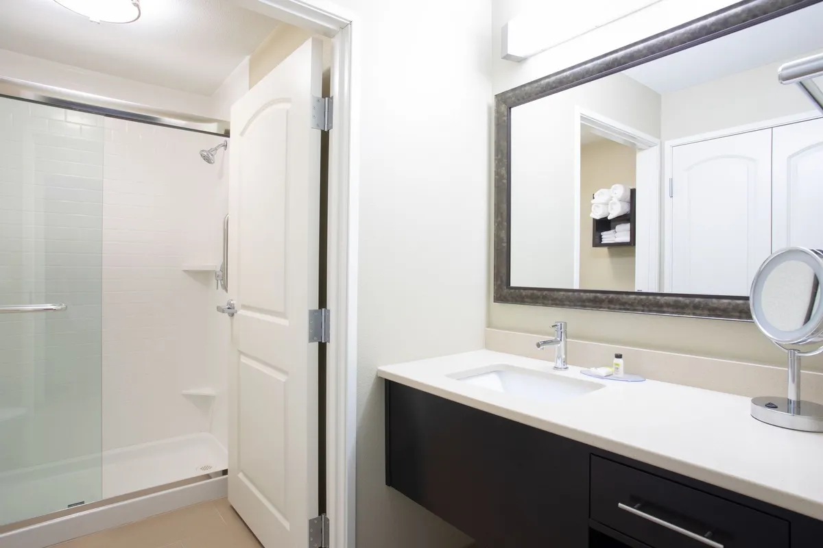 A modern bathroom with a sleek walk-in shower, a vanity topped with fresh towels, and a large mirror. The finishes are contemporary, and the overall design feels clean, fresh, and welcoming—ideal for moments of relaxation and self-care.