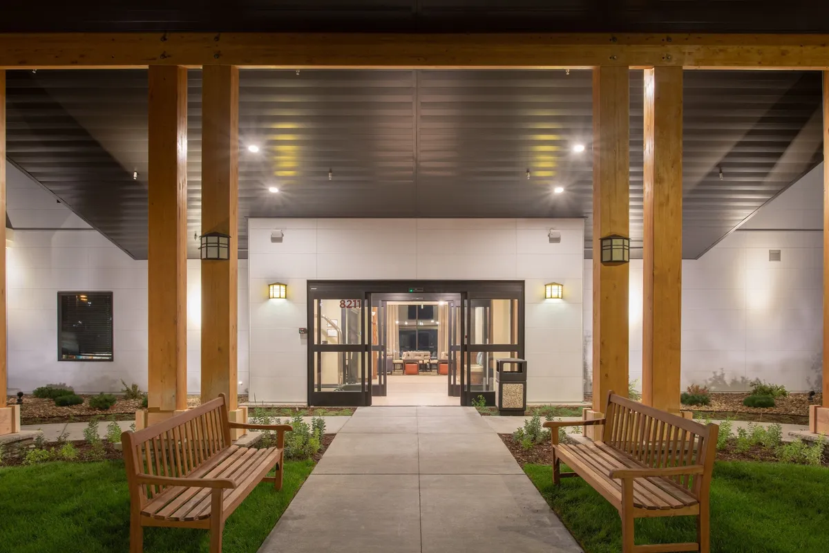 A welcoming exterior view of the property's entrance, framed by thoughtfully landscaped greenery and comfortable benches. The scene invites guests to relax or gather before heading out to explore or attend meetings, capturing the approachable, business-friendly atmosphere emphasized in the section.