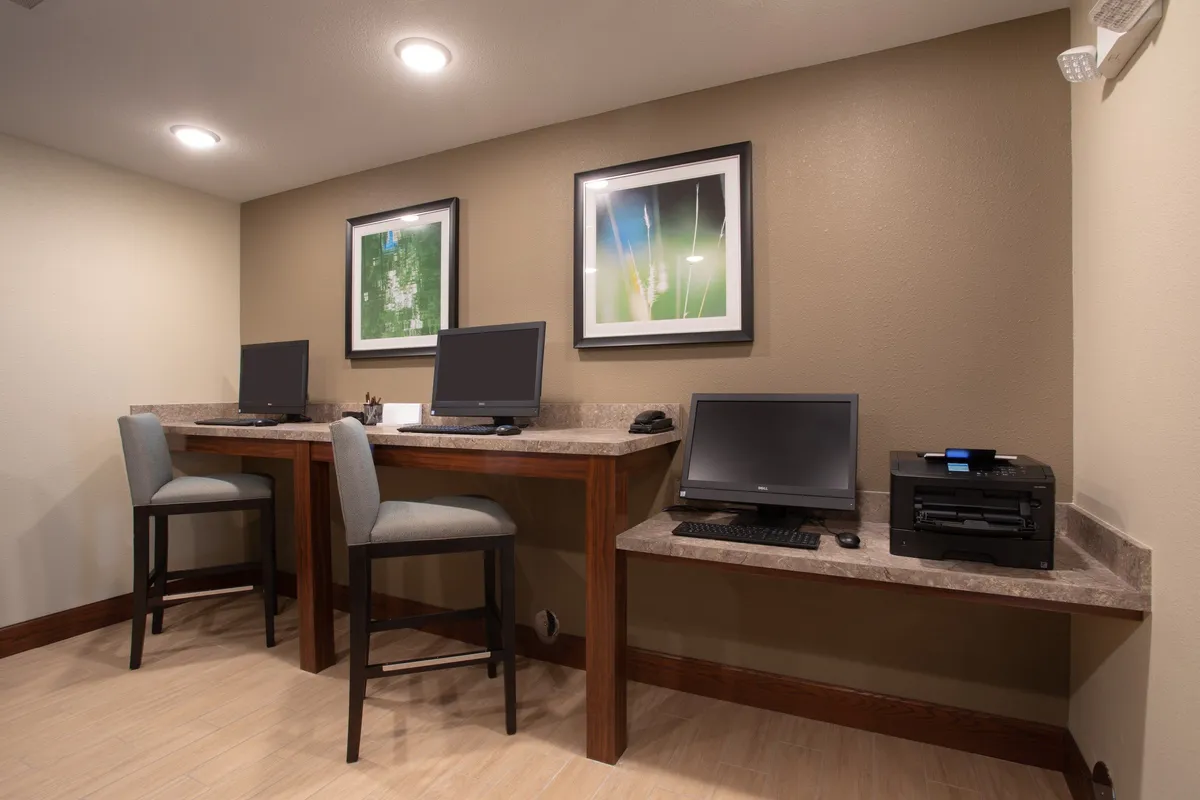 A focused workspace featuring computers, a printer, and wall artwork, set within a practical and distraction-free environment. The layout encourages productivity and supports business needs such as printing or internet browsing.